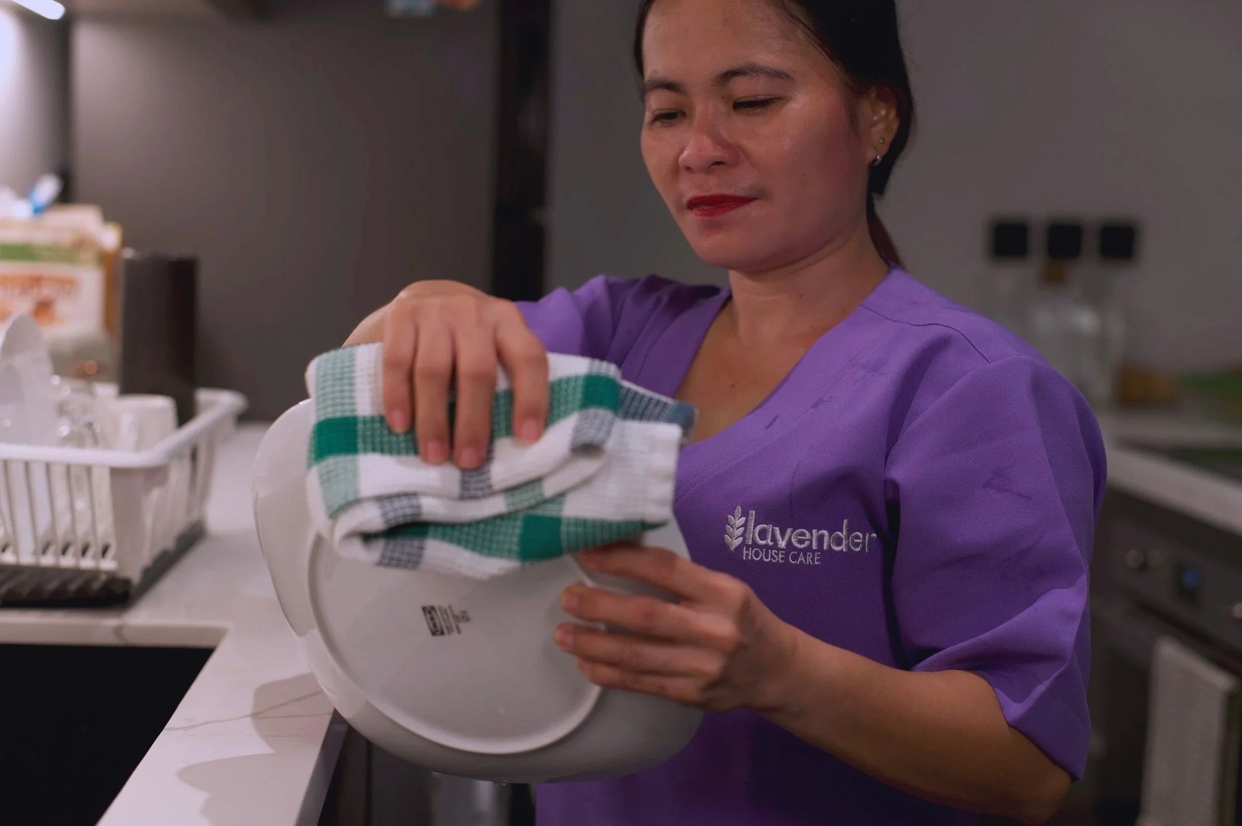 Part-time maid from the Philippines is carefully cleaning a plate in Lavender Housecare uniform.